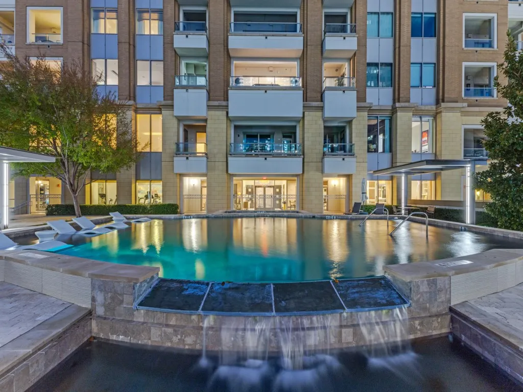 Infinity-edge pool with integrated waterfall feature, surrounded by stone-clad hardscaping