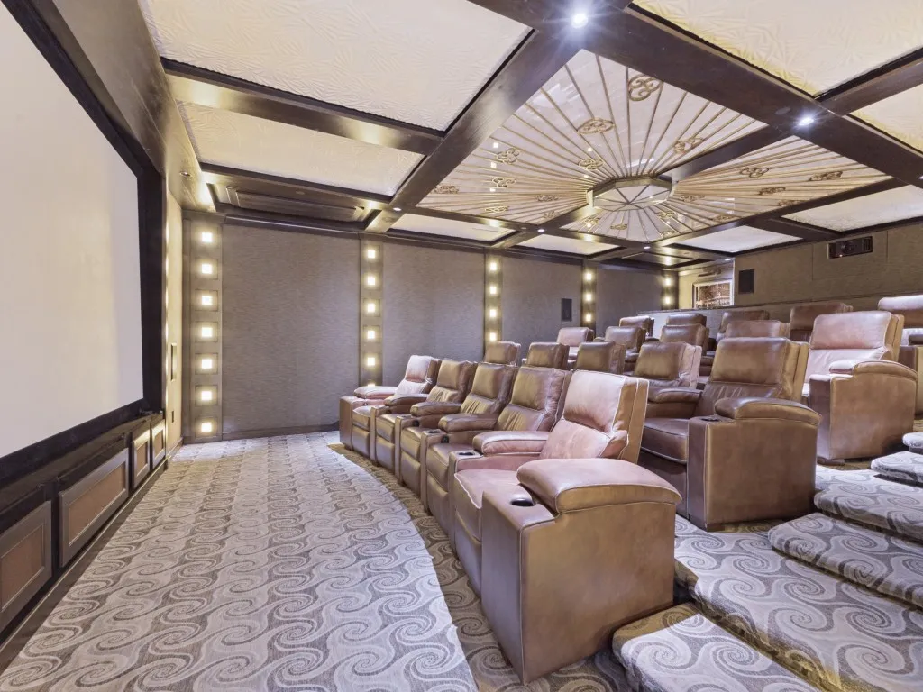 Dedicated home theater with tiered seating, large projection screen, and patterned wall-to-wall carpeting