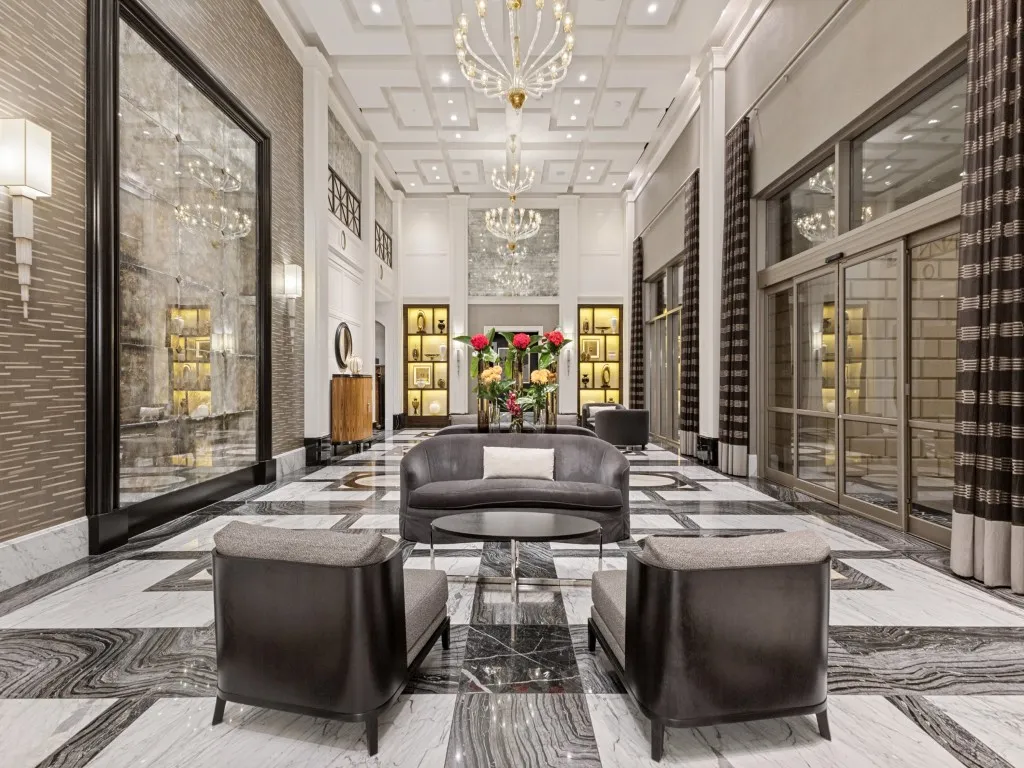 Coffered ceiling with multiple chandeliers, full-height wall mirror, illuminated display shelving, floor-to-ceiling glass paneling, and patterned tile flooring