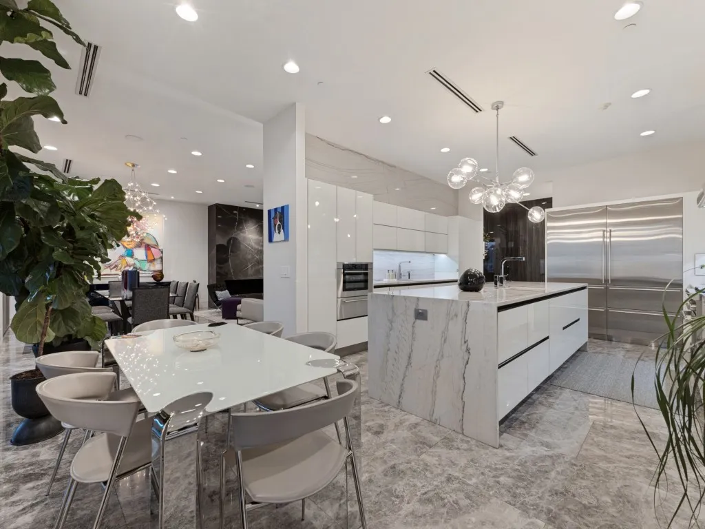 Modern kitchen featuring high-gloss cabinetry, a central waterfall-edge island, stone-surfaced countertops, integrated stainless steel appliances, and recessed lighting