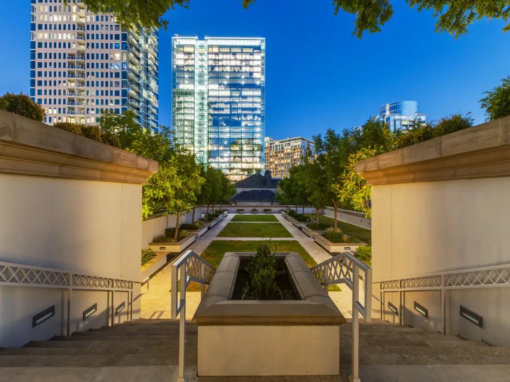 Tiered outdoor space featuring a central lawn, mature plantings, and integrated lighting within concrete walls