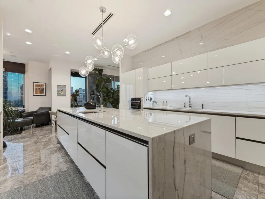 Gourmet kitchen with a waterfall island, sleek white cabinetry, integrated sink, recessed lighting, and a contemporary chandelier