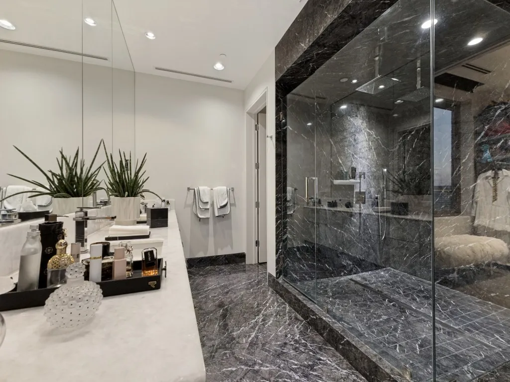 Spacious bathroom featuring a dual vanity, floor-to-ceiling mirrors, recessed lighting, and a large walk-in shower with dark marbled walls and flooring