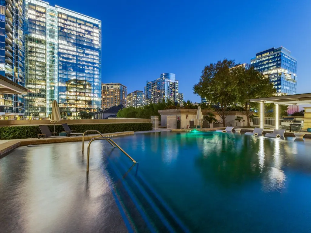Rooftop swimming pool with built-in lounge seating, surrounded by architectural landscaping and contemporary high-rise buildings