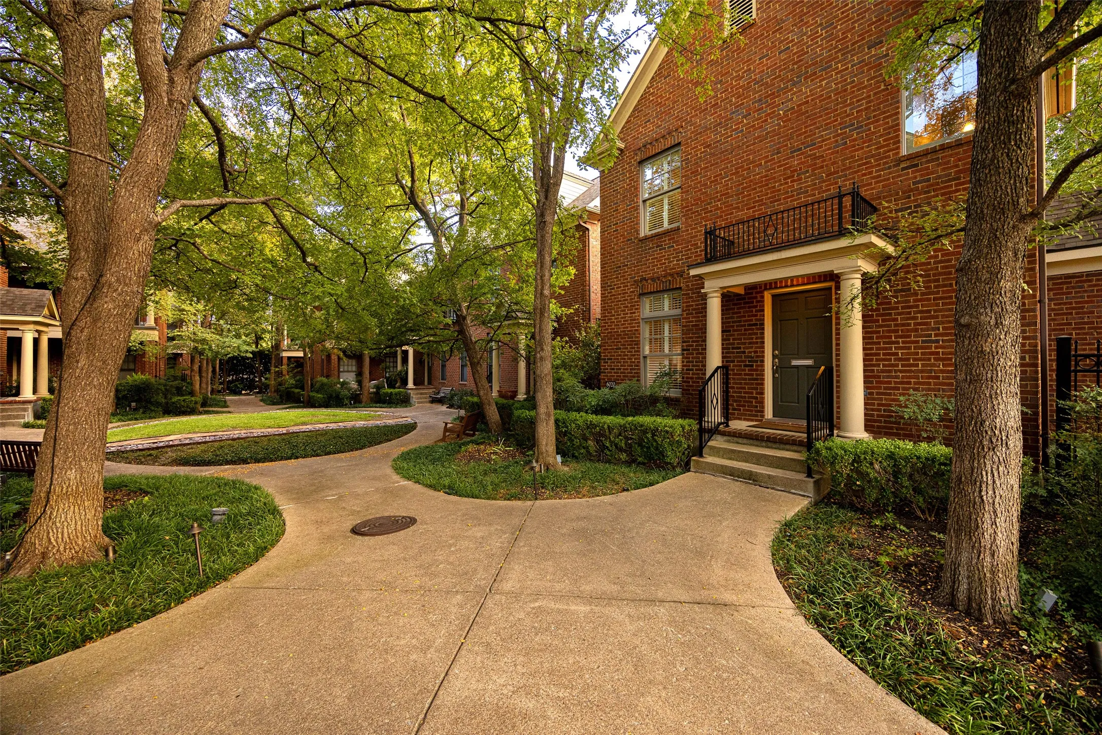 Classic brick exterior featuring a covered portico, decorative iron balcony railing, stately columns, and mature landscaping