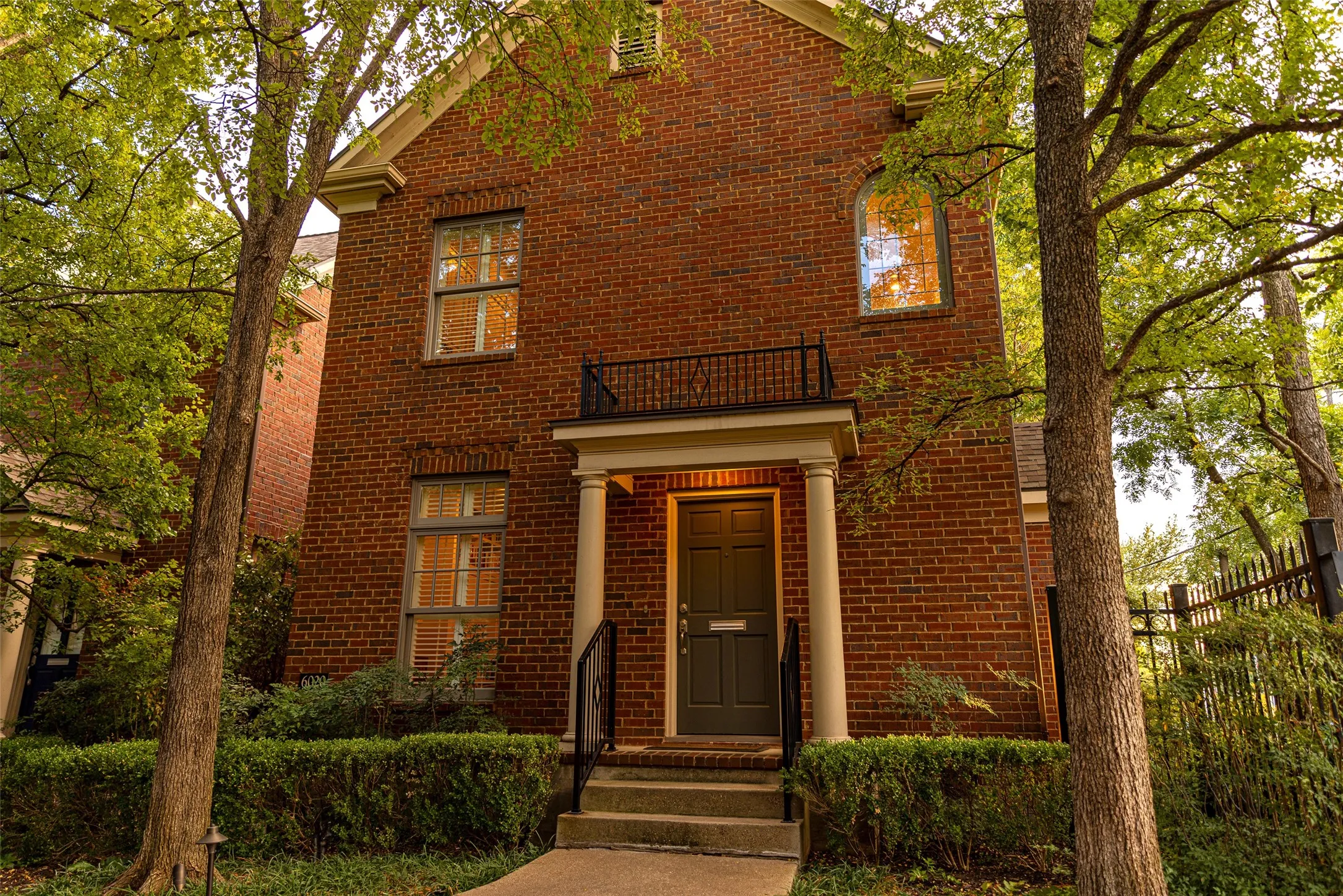 Traditional brick exterior featuring a covered entryway with classical columns, a second-story wrought iron balcony, and arched window detailing