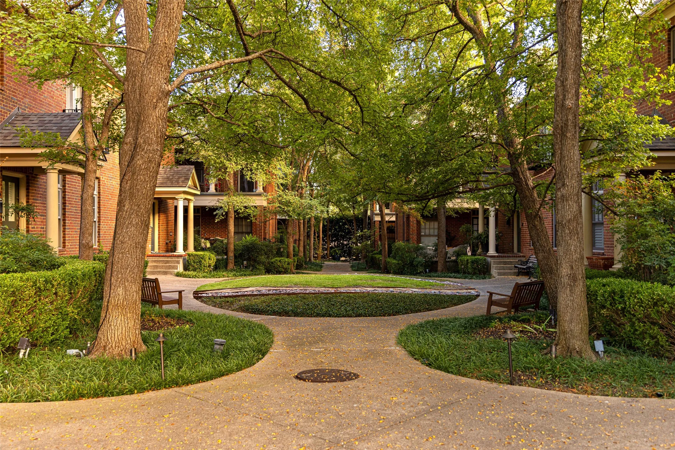 Courtyard featuring brick exterior facades, architectural columns, paved pathways, mature canopy trees, and manicured landscaping