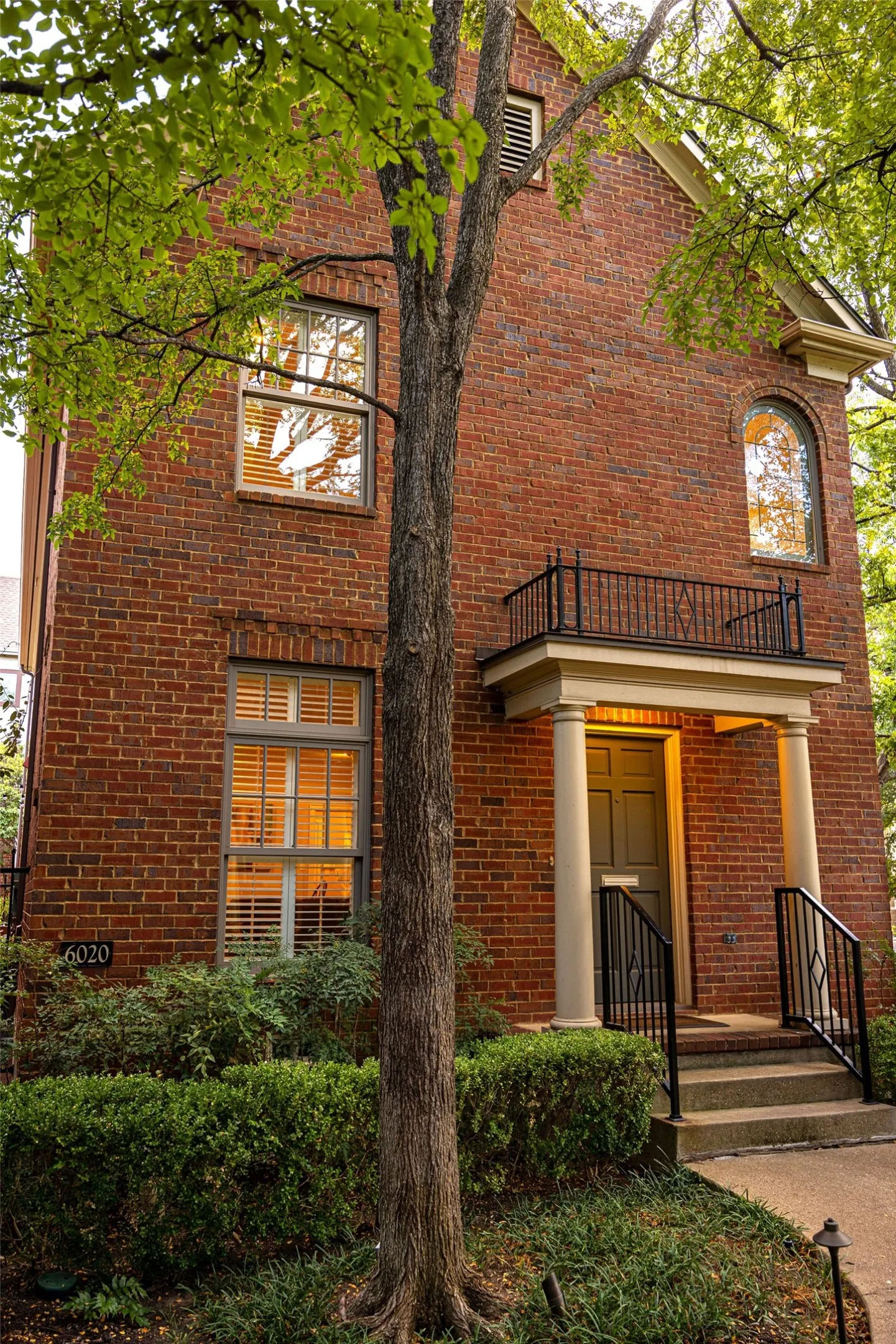 Two-story brick exterior featuring a covered entryway with columns, a wrought-iron Juliet balcony, and a prominent arched window