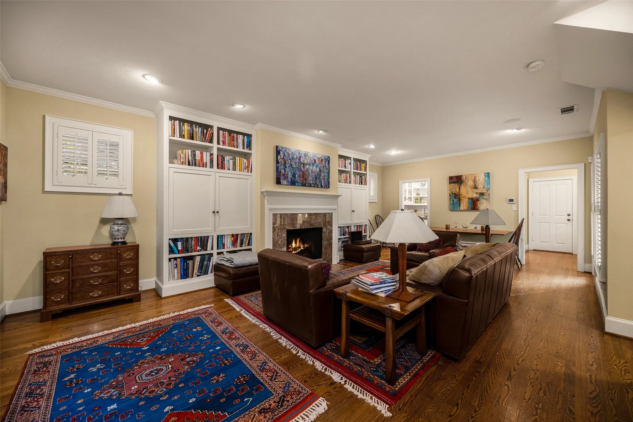 Living area featuring hardwood flooring, recessed lighting, and a fireplace with a stone-surround mantel flanked by floor-to-ceiling custom built-in cabinetry