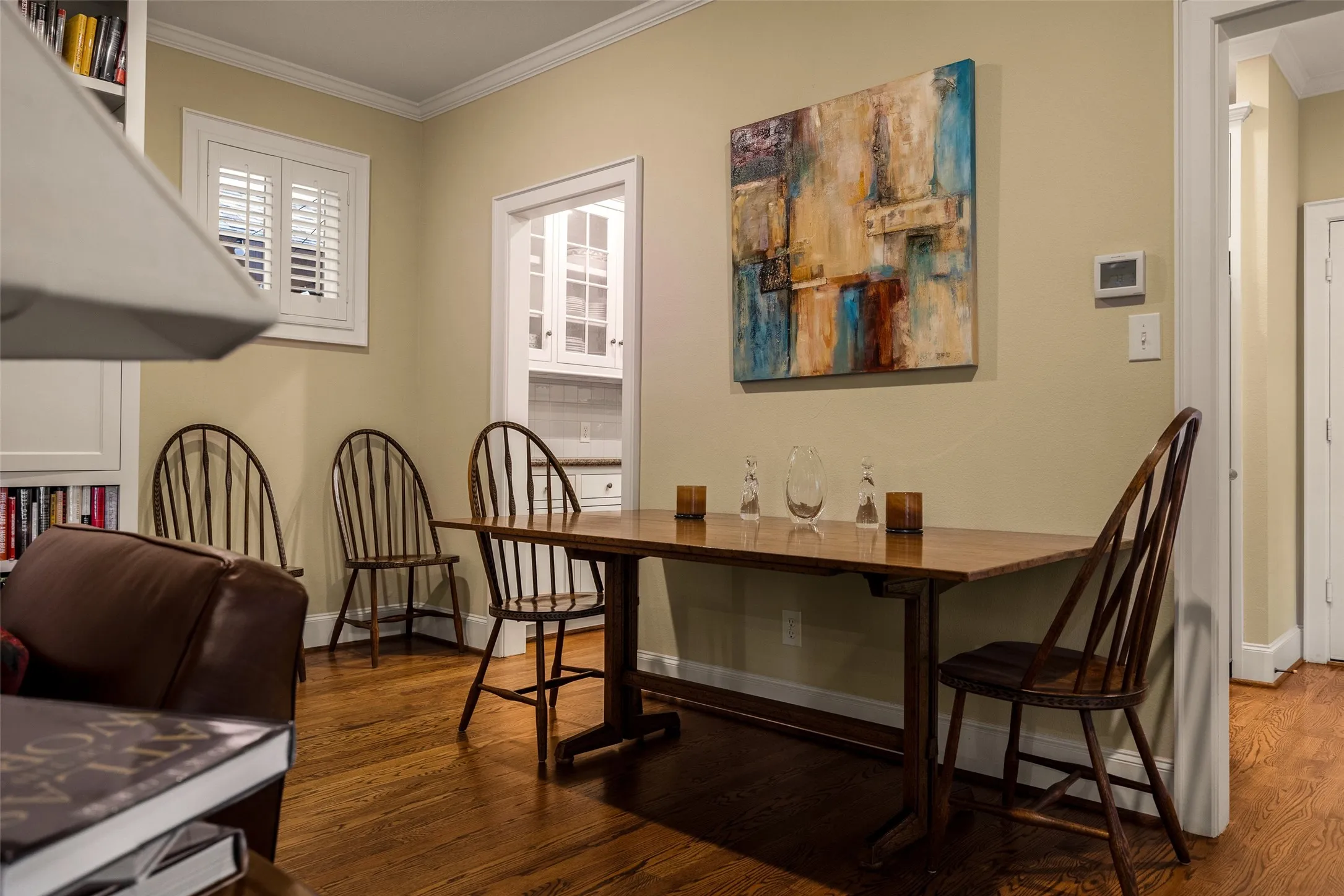 Interior space featuring polished wood-finish flooring, built-in shelving, white plantation shutters, and crown molding