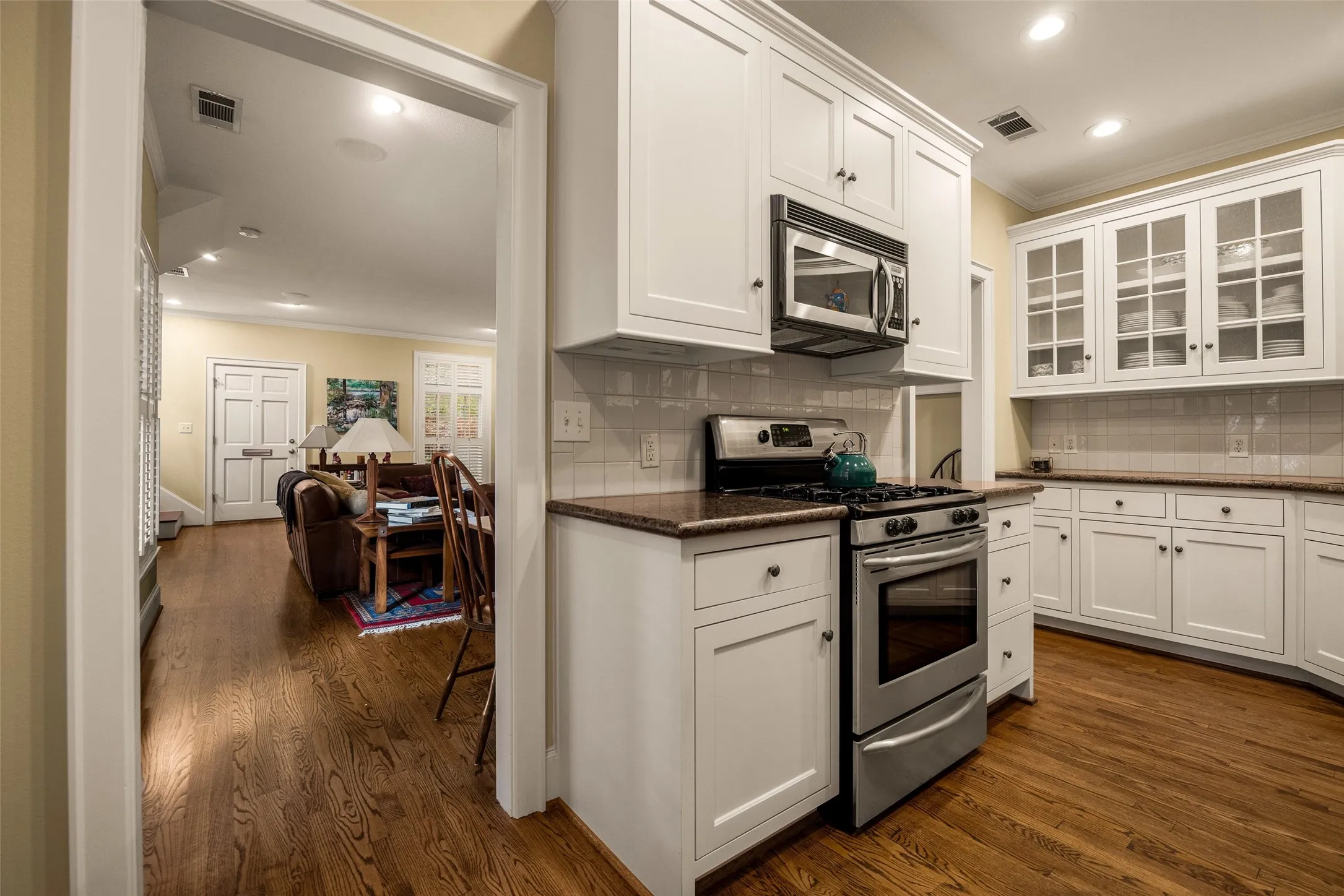 Kitchen featuring white shaker-style cabinetry, stainless steel appliances, glass-front upper cabinets, stone-surfaced countertops, and wood-finish flooring