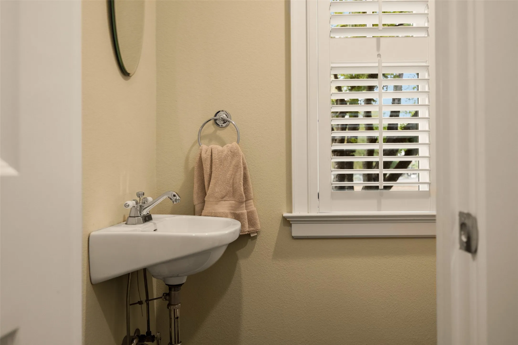 Wall-mounted ceramic pedestal sink, chrome hardware, and white plantation shutters