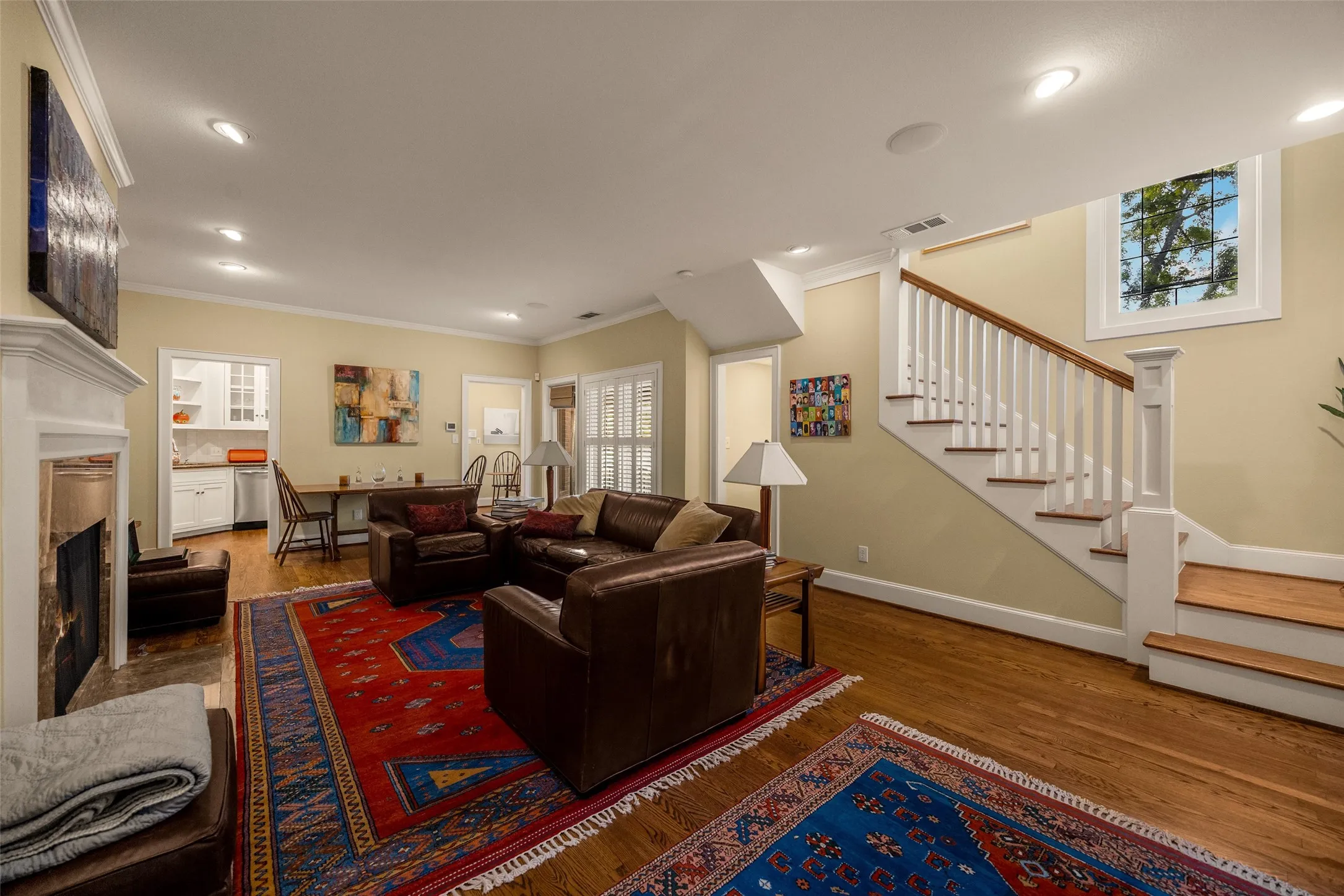Living area featuring wood-finish flooring, a fireplace with a decorative mantel, recessed lighting, and a staircase with white balusters and wood treads
