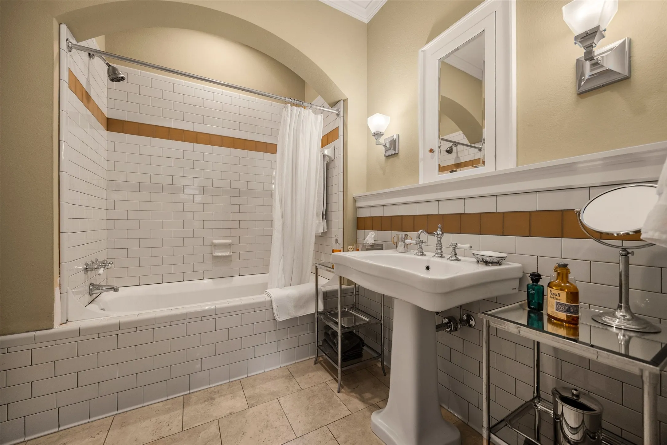 Bathroom featuring a pedestal sink, arched shower alcove, subway tile walls with horizontal decorative accents, and tiled flooring