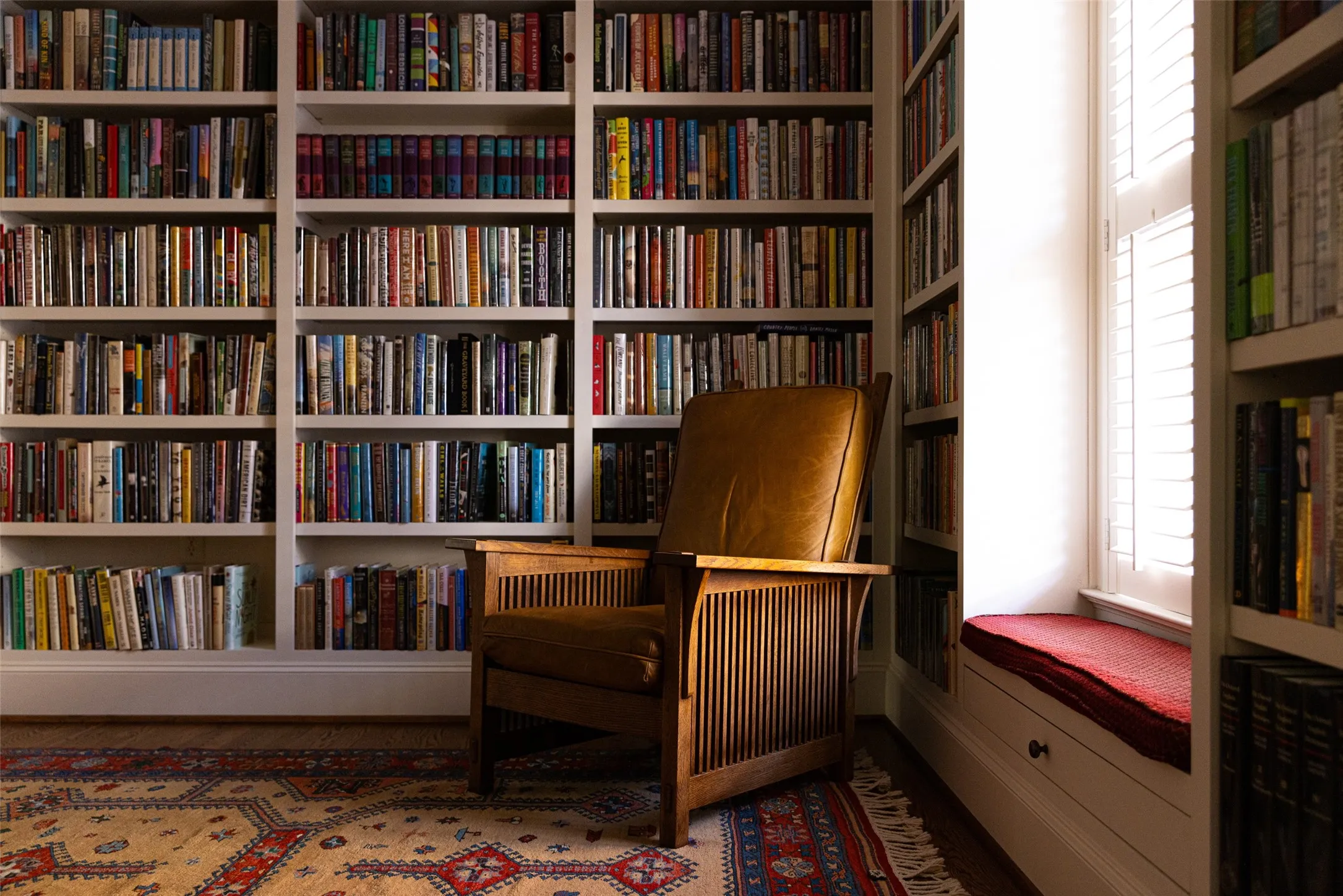 Floor-to-ceiling built-in wooden shelving units with integrated window seat featuring a lower storage drawer