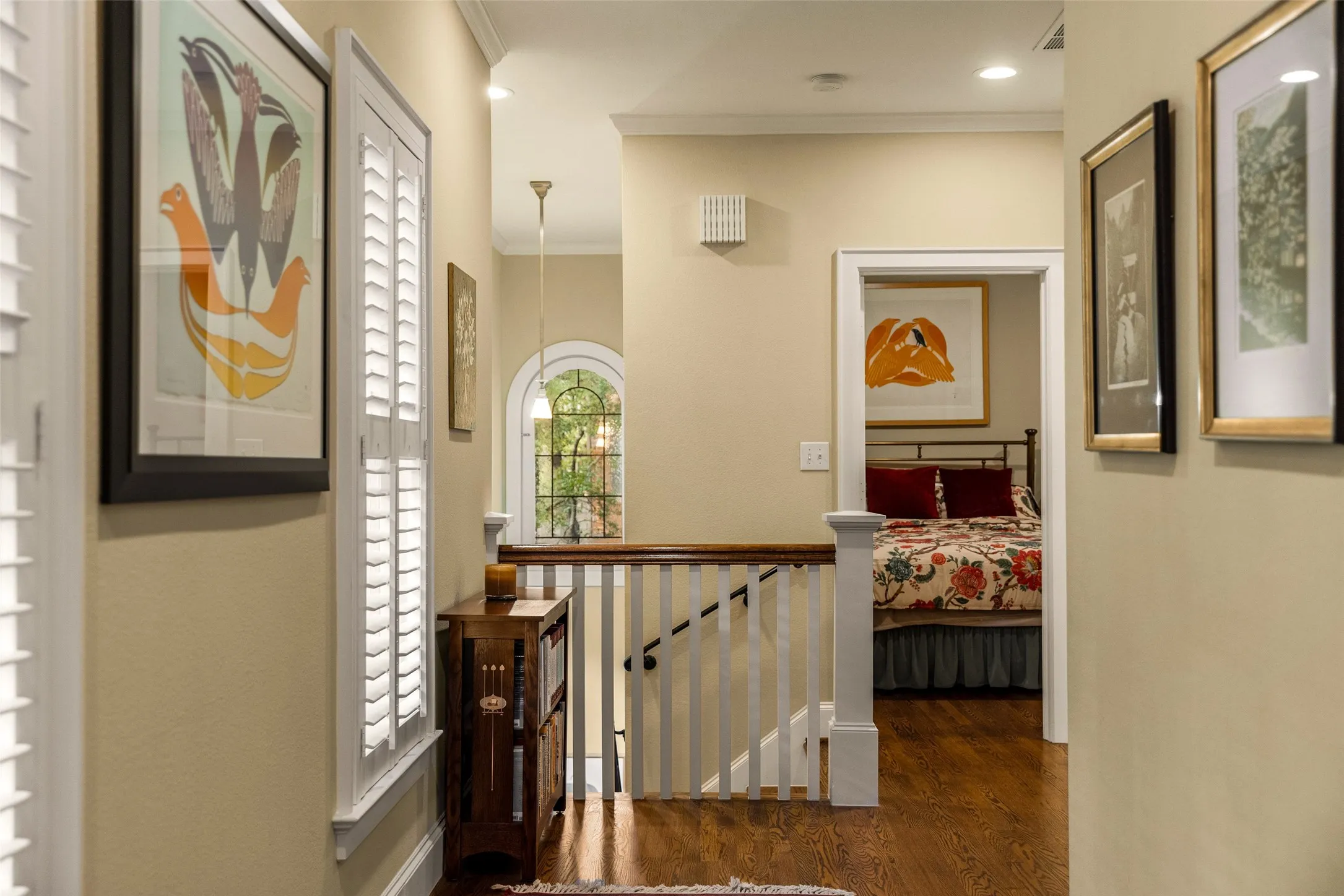 Wood-finish flooring, arched window with multi-pane glass, white-painted wood balustrade, and plantation shutters