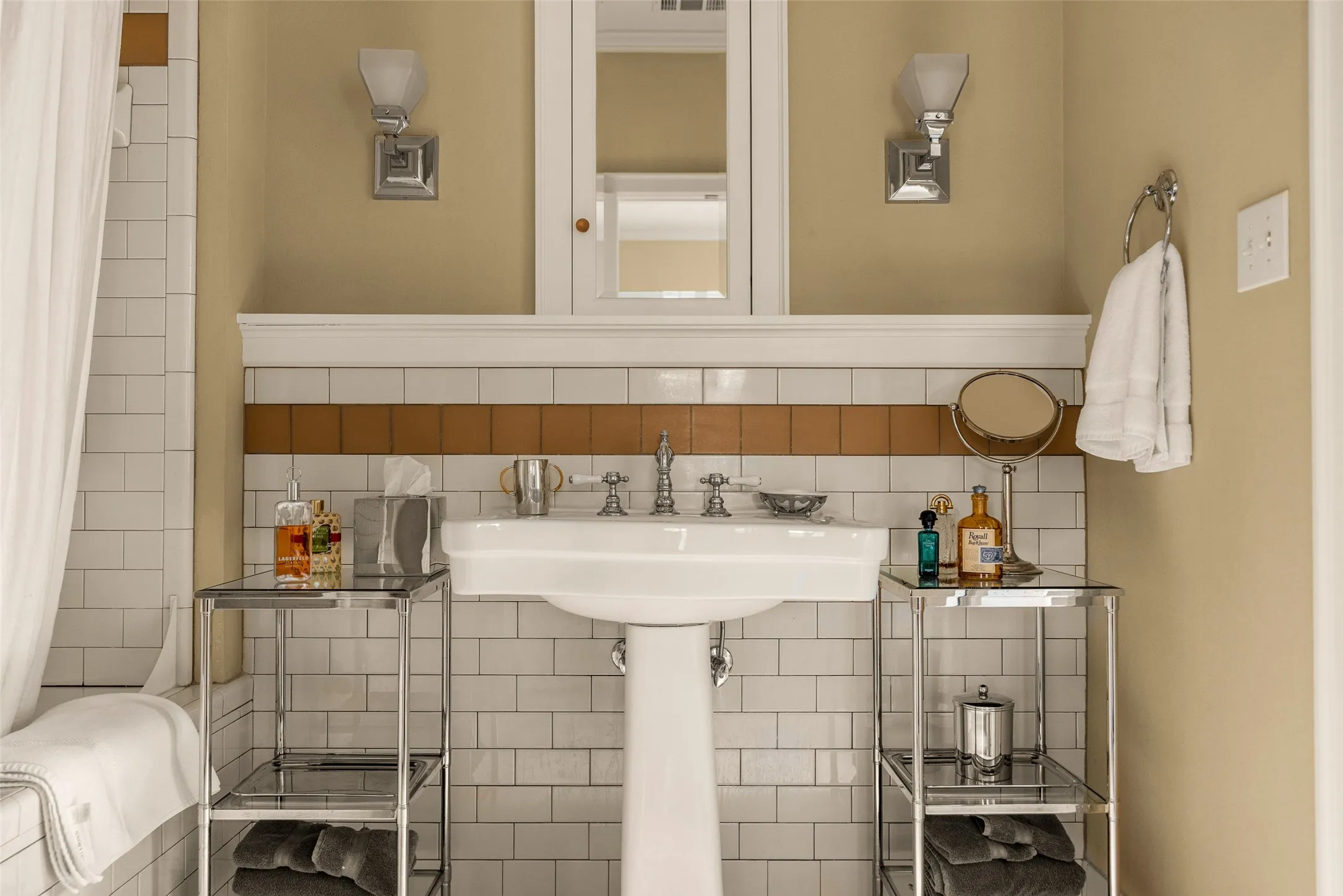 Pedestal sink featuring chrome widespread faucet hardware, subway tile wall cladding with a decorative tile accent band, built-in medicine cabinet, and dual wall-mounted light fixtures