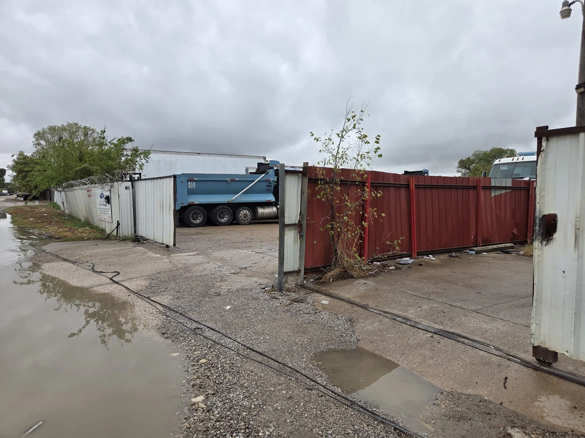 Industrial property featuring a gated entry, concrete paving, and perimeter metal fencing topped with security wire