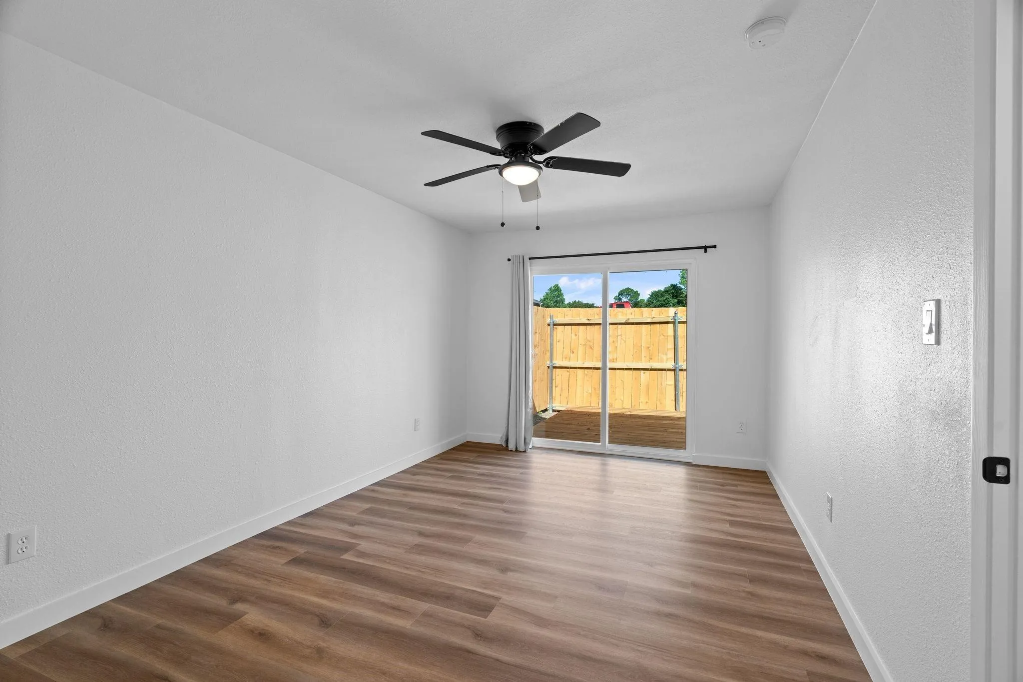 Interior space featuring wood-finish flooring, white walls, a ceiling fan with integrated lighting, and a sliding glass door providing external access