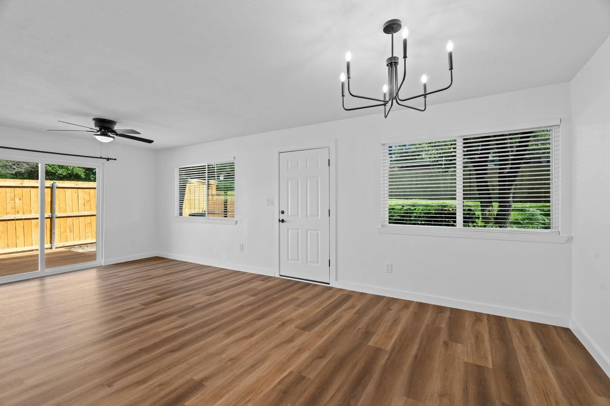 Living space featuring wood-finish flooring, a contemporary six-arm chandelier, ceiling fan, and sliding glass door access to the exterior
