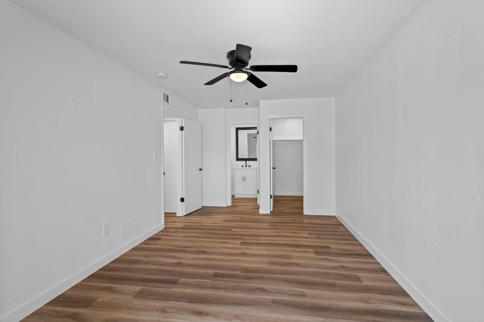 Neutral interior featuring wood-finish flooring, a central ceiling fan with integrated lighting, and white walls