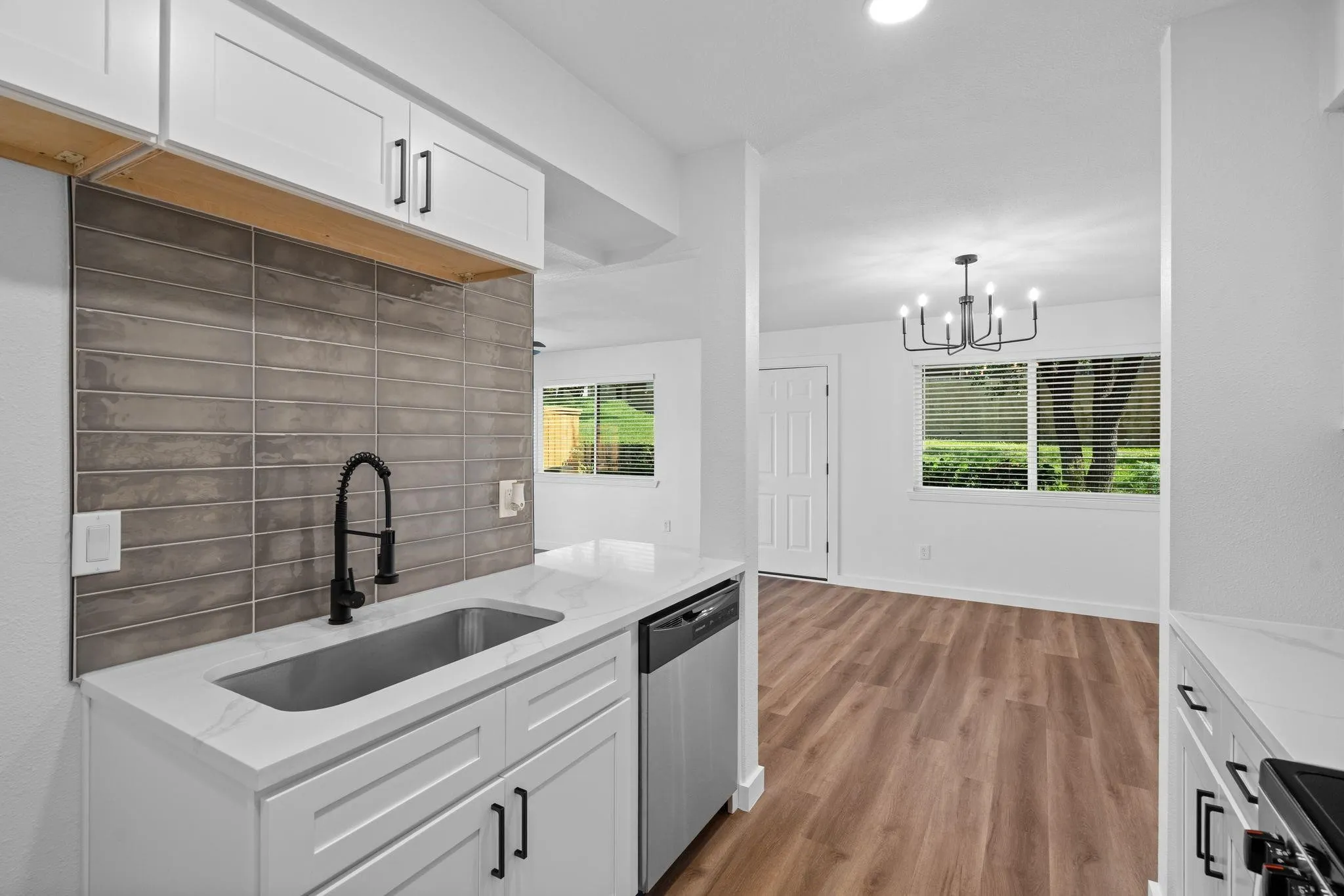 Kitchen featuring white shaker-style cabinetry, quartz countertops, a grey tile backsplash, stainless steel undermount sink with a matte black pulldown faucet, and wood-finish flooring
