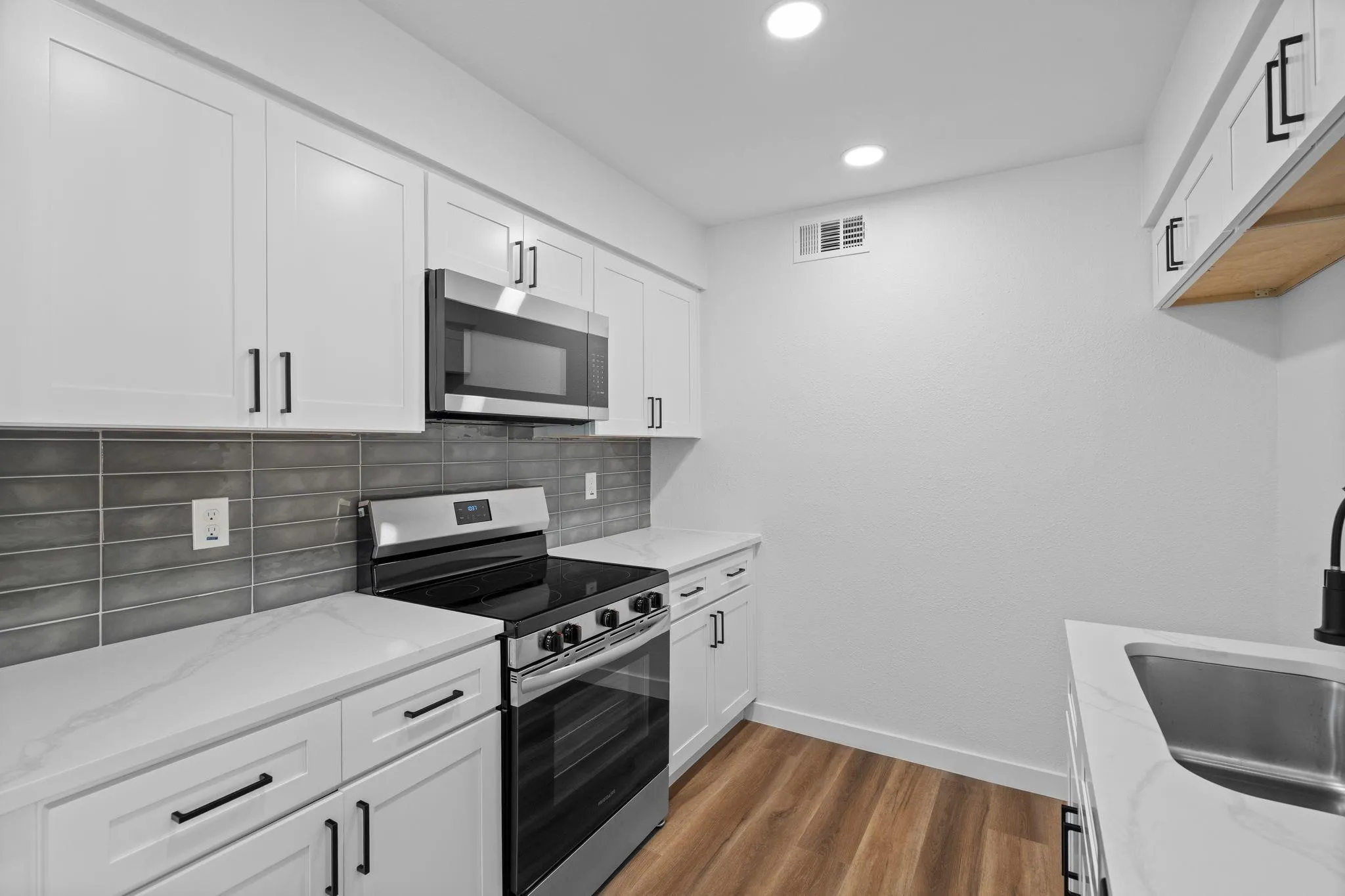 Kitchen featuring white shaker-style cabinetry, quartz countertops, gray subway tile backsplash, stainless steel appliances, and wood-finish flooring