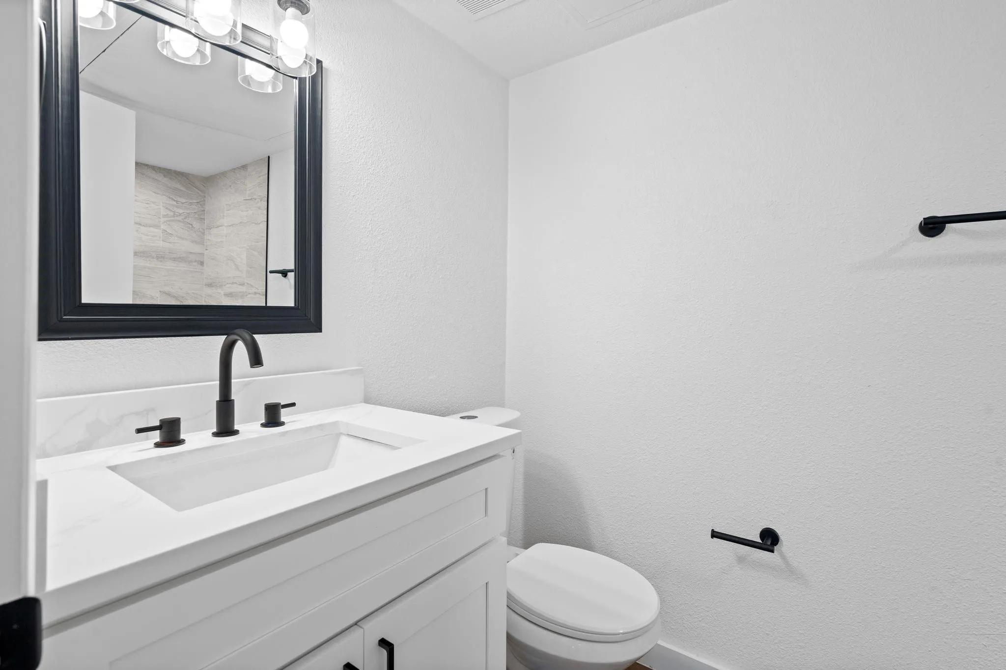 White vanity featuring a white countertop with an integrated rectangular sink, matte black widespread faucet, black-framed mirror, and matching matte black hardware