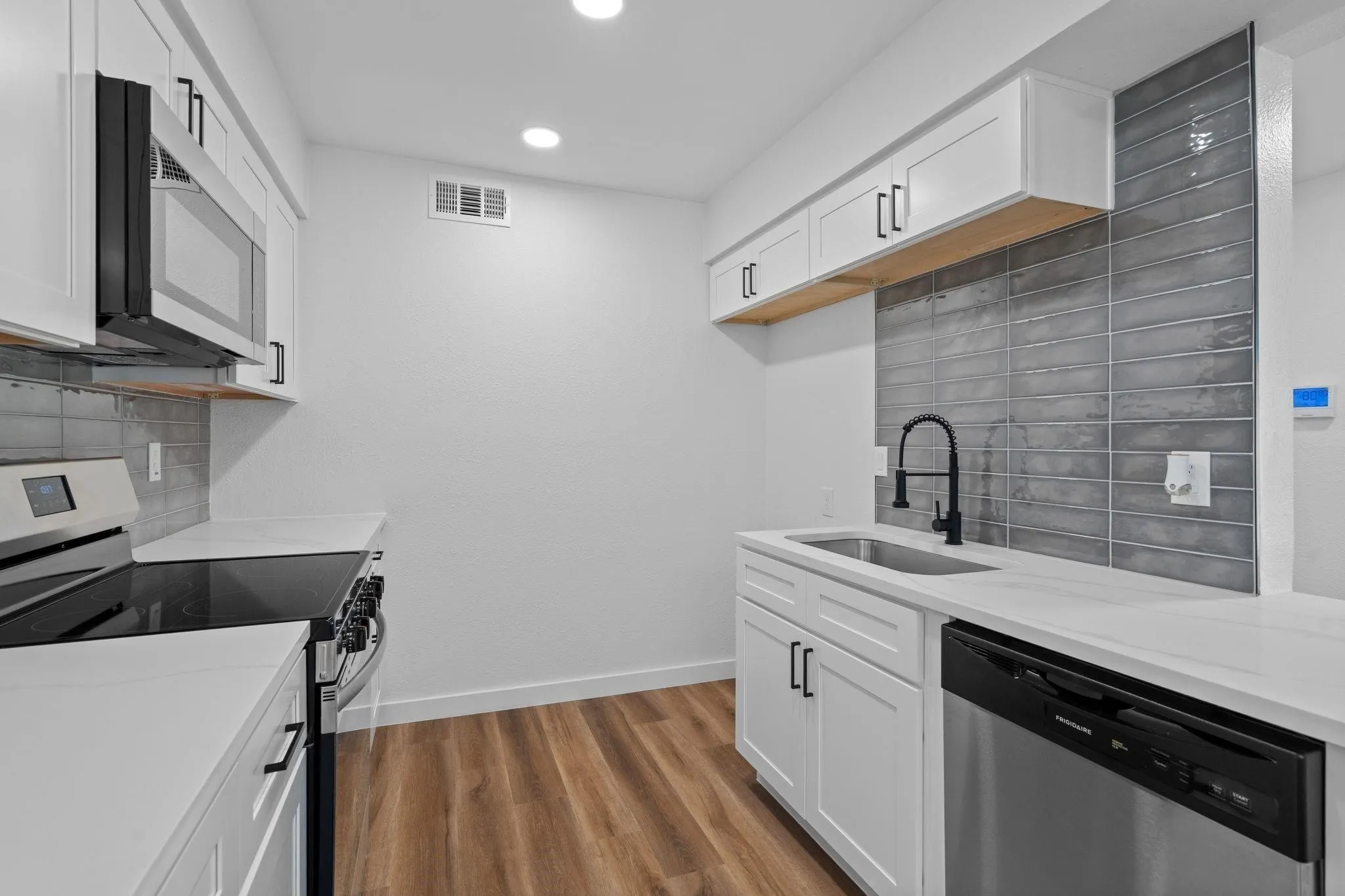 Kitchen featuring white shaker-style cabinetry, white countertops, gray elongated tile backsplash, stainless steel appliances, and wood-finish flooring