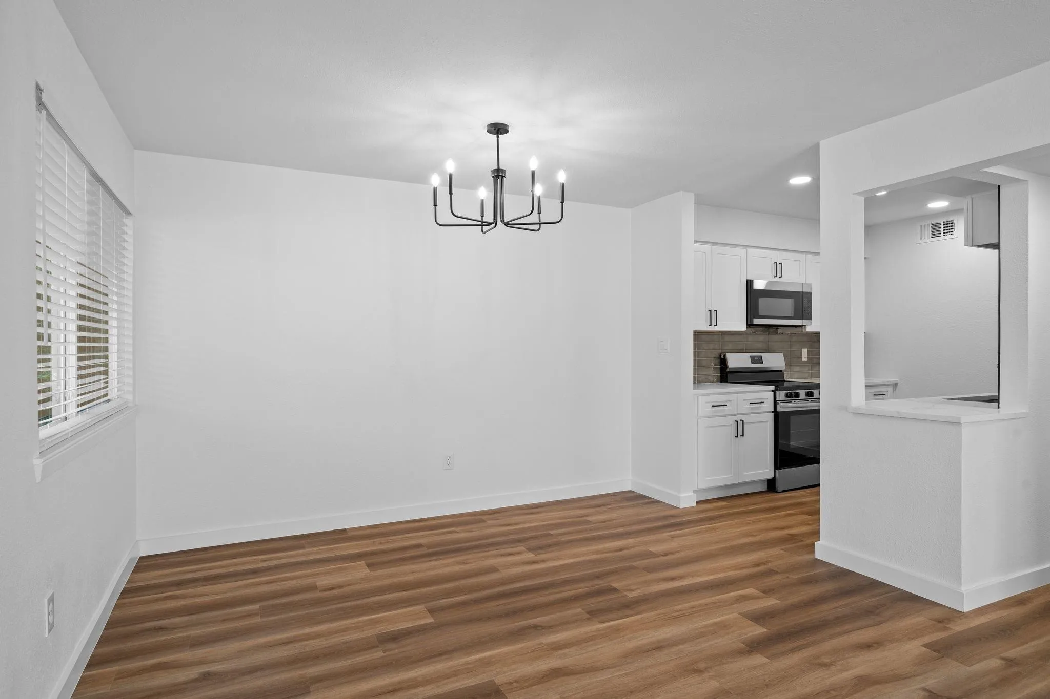 Open-concept space featuring wood-finish flooring, a modern multi-arm chandelier, white cabinetry, and a pass-through counter