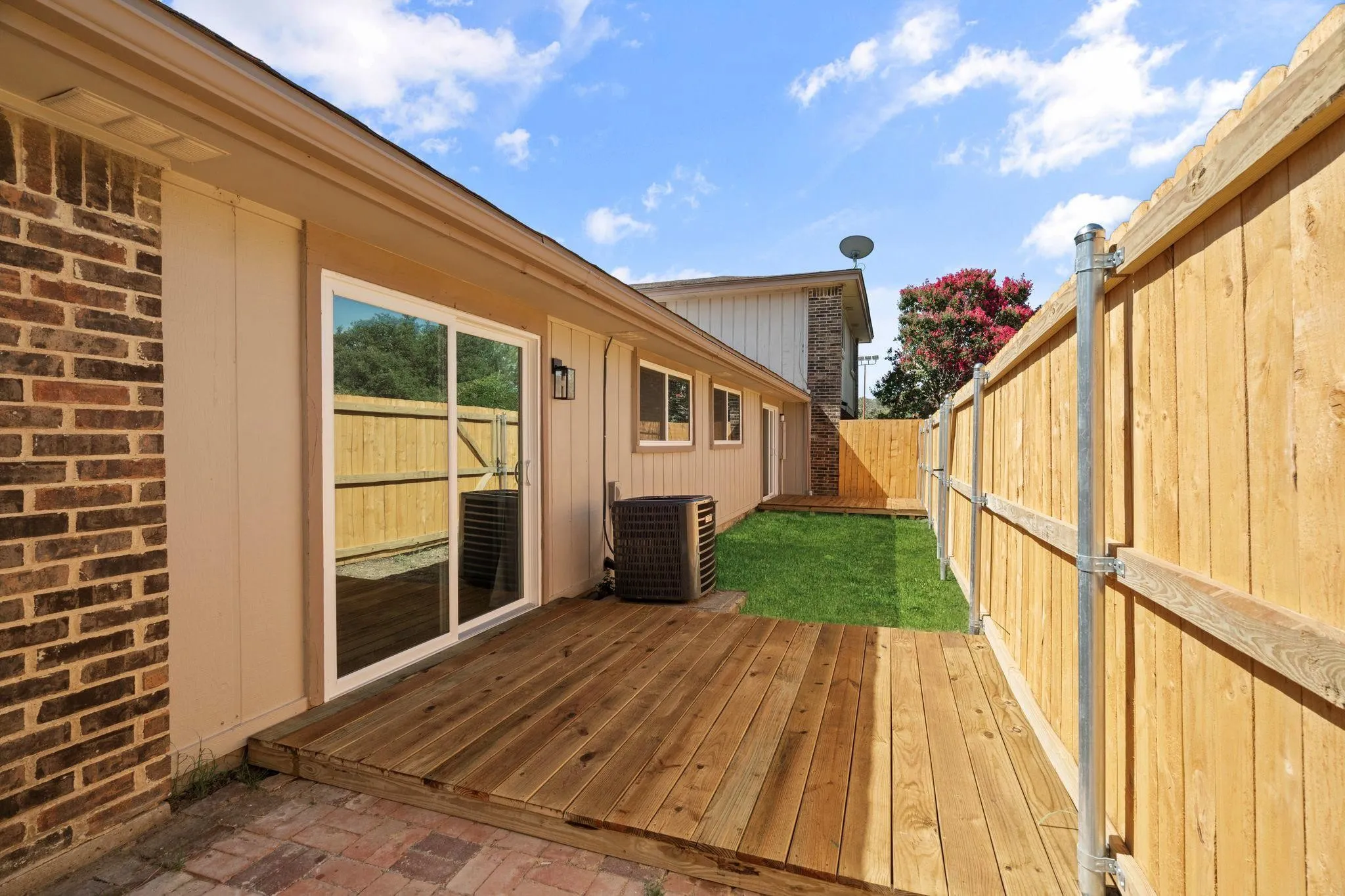 Rear exterior featuring a wood deck, brick and siding facade, sliding glass door, and wood privacy fencing