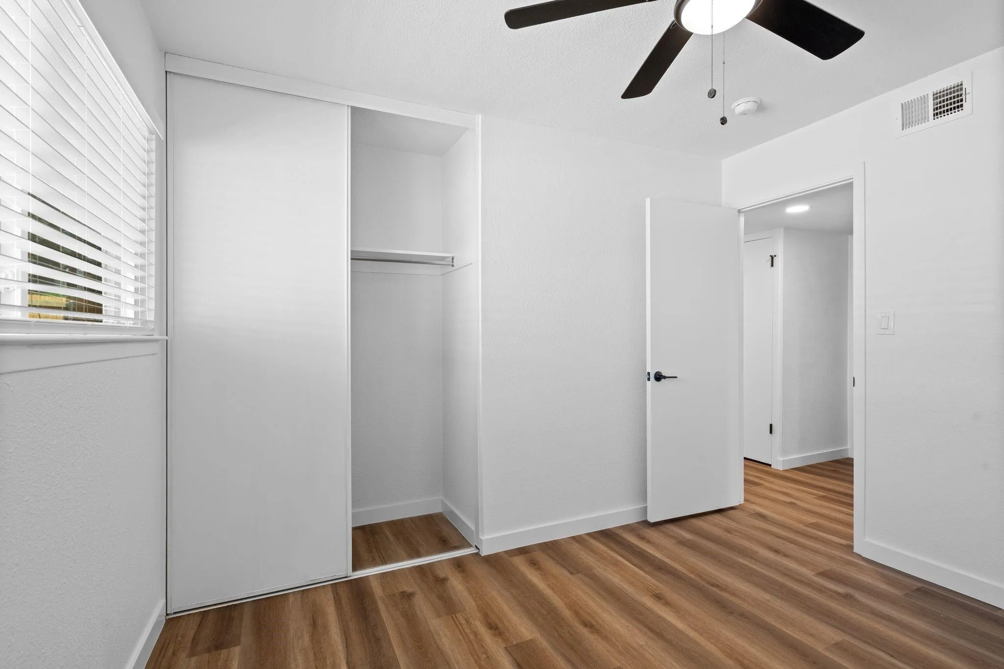 Room featuring wood-finish flooring, sliding door closet with built-in shelving, ceiling fan with integrated lighting, and horizontal blinds