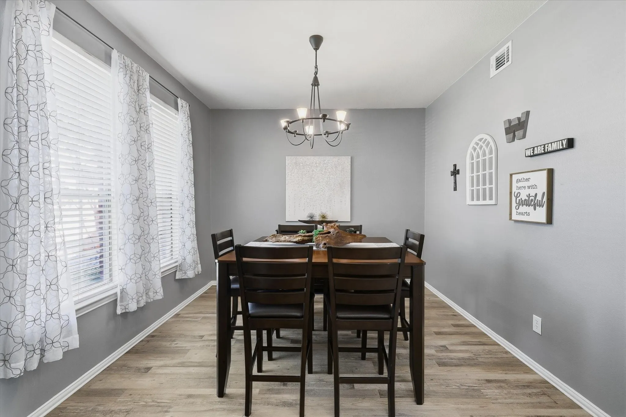 Tall windows bring natural light into the dining room, complemented by a chandelier & luxury vinyl plank flooring.