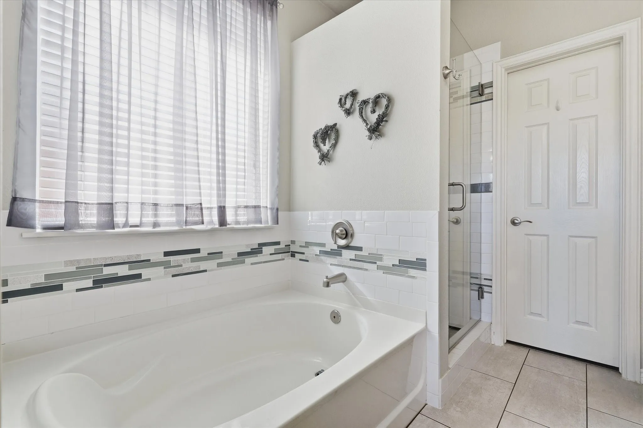 A soaking tub beneath a large window offers a relaxing spot, with decorative tile continuing into the separate shower.