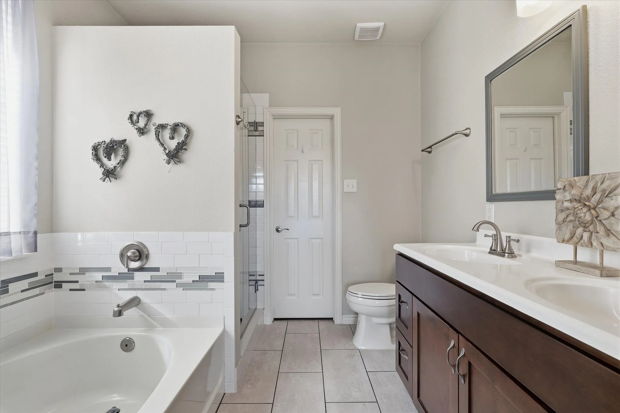 The updated primary bath brings together a soaking tub, double-sink vanity & separate glass-enclosed shower.