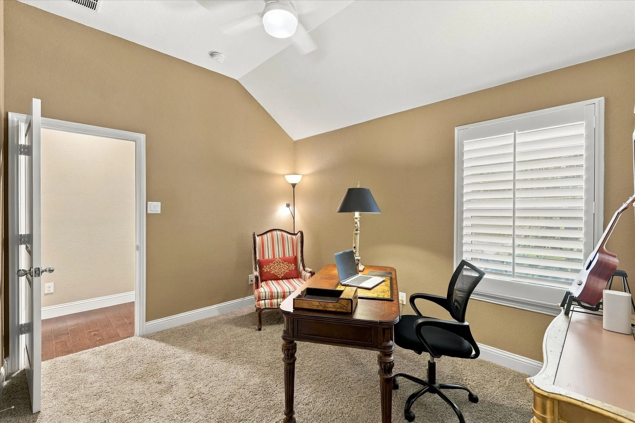 Vaulted ceiling with integrated paddle Secluded guest bedroom that is split from rest of home, currently used as second office with a walk in closet. , carpeted flooring, and plantation shutters