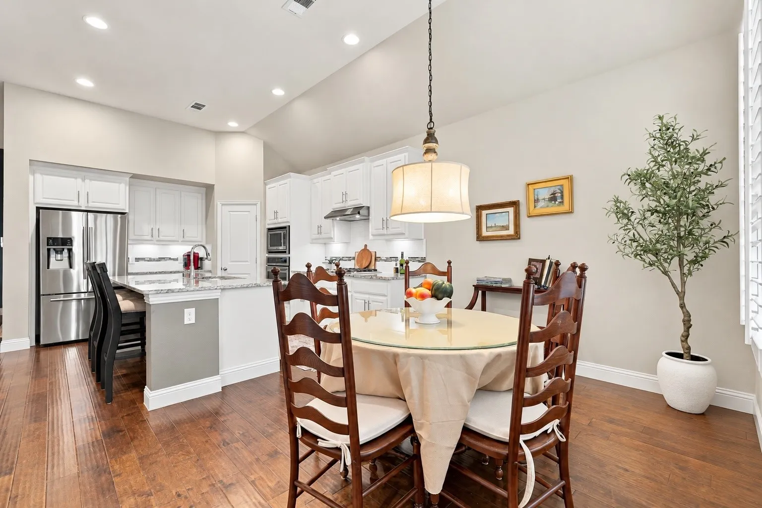 Kitchen featuring white shaker-style cabinetry, stone countertops, stainless steel appliances, a vaulted ceiling, and wood-finish flooring