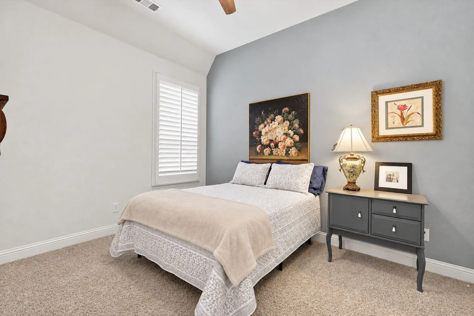 Bedroom featuring vaulted ceilings, neutral carpeting, an accent wall, and interior window shutters