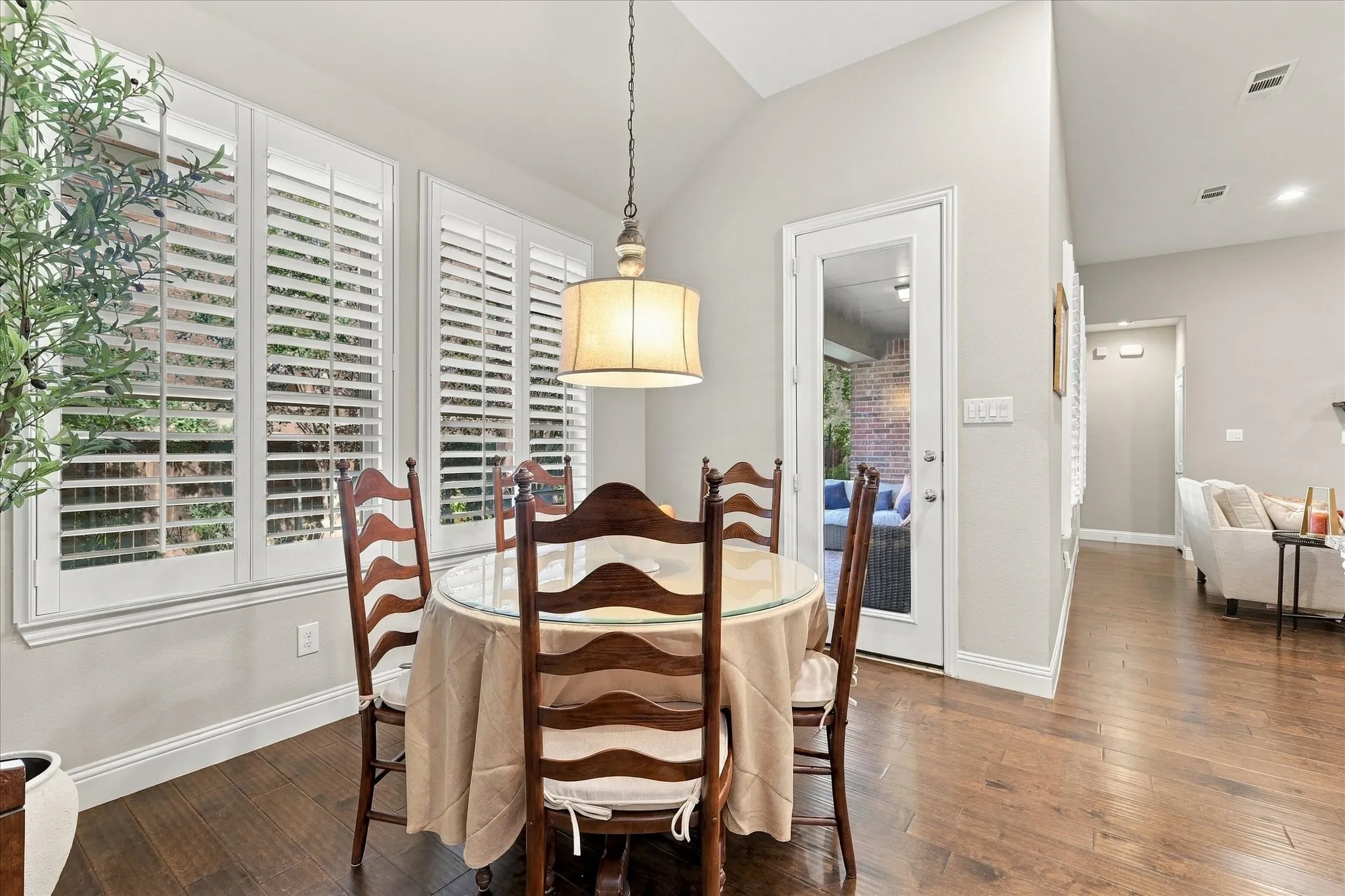 Vaulted ceiling, wood-finish flooring, plantation shutters, and a drum-style pendant light fixture