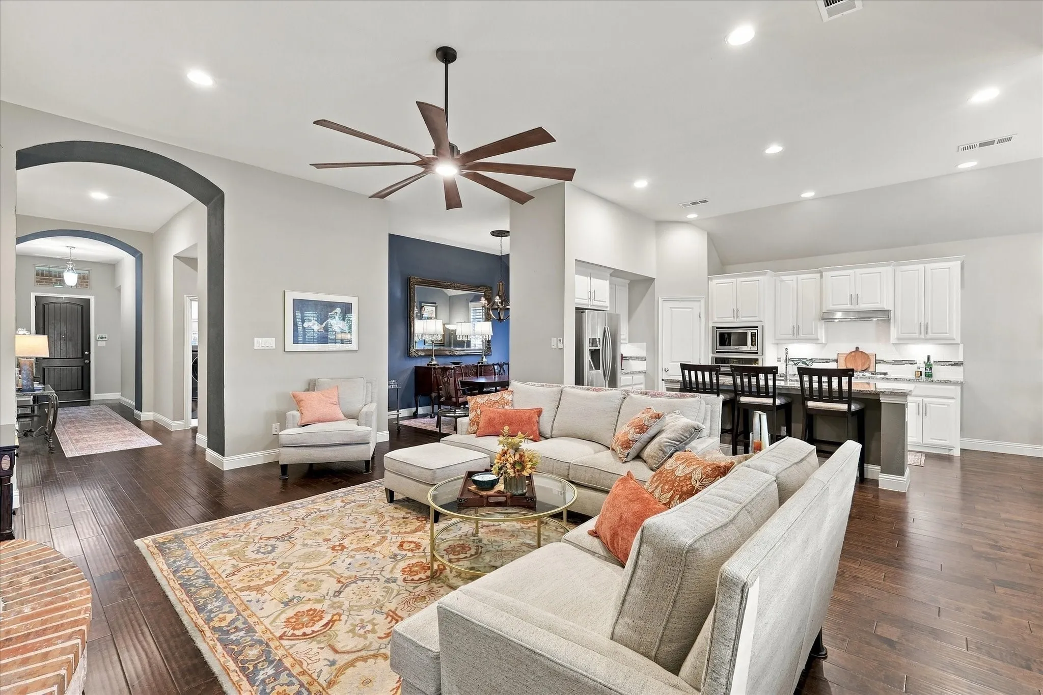 Open-concept living space featuring wood-finish flooring, vaulted ceilings, a large multi-blade ceiling fan, recessed lighting, and kitchen cabinetry with built-in stainless steel appliances
