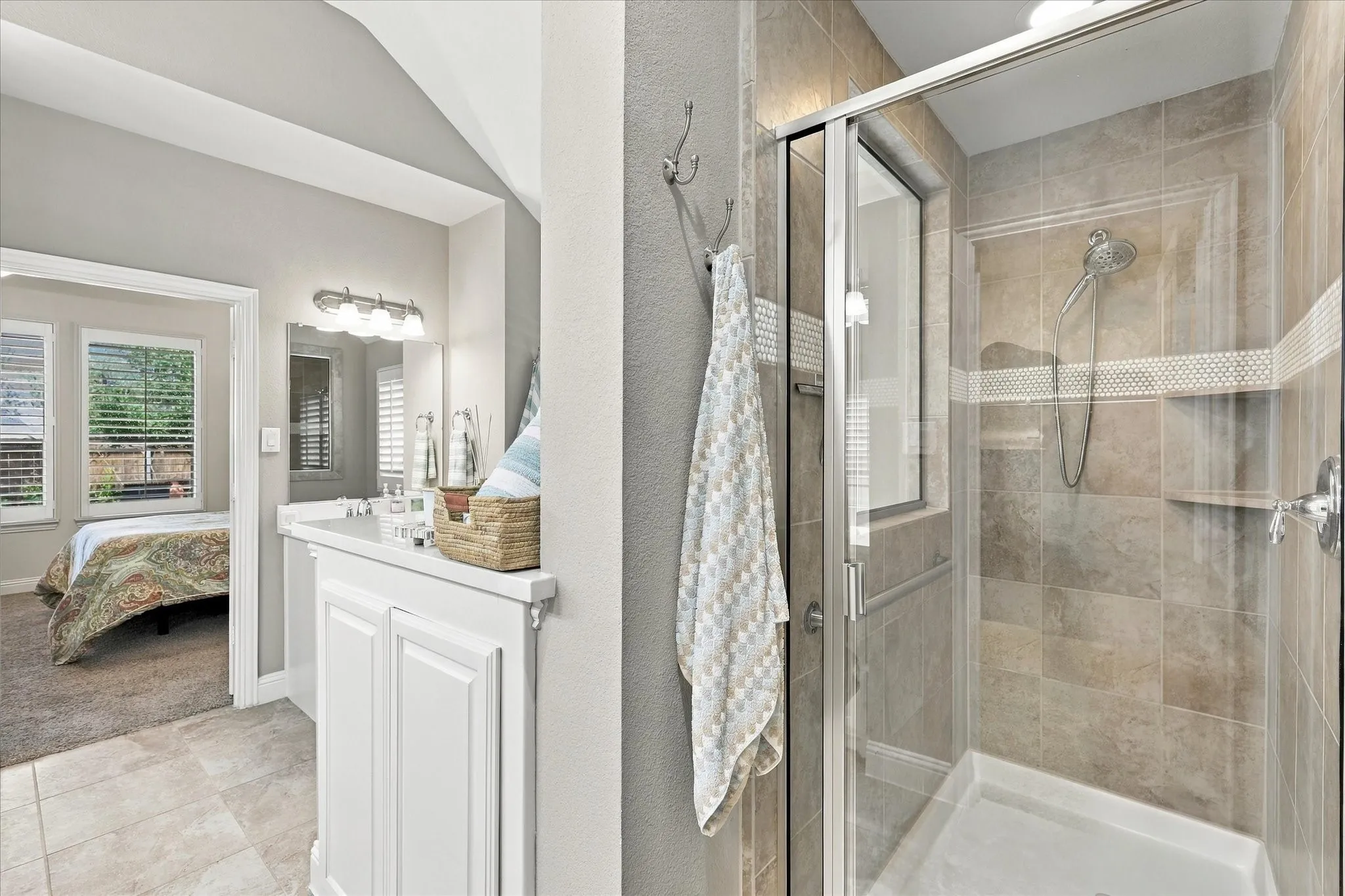 Bathroom featuring a walk-in shower with tile surround, mosaic tile accent border, glass enclosure, and built-in shelving, paired with a white vanity cabinet and vaulted ceiling