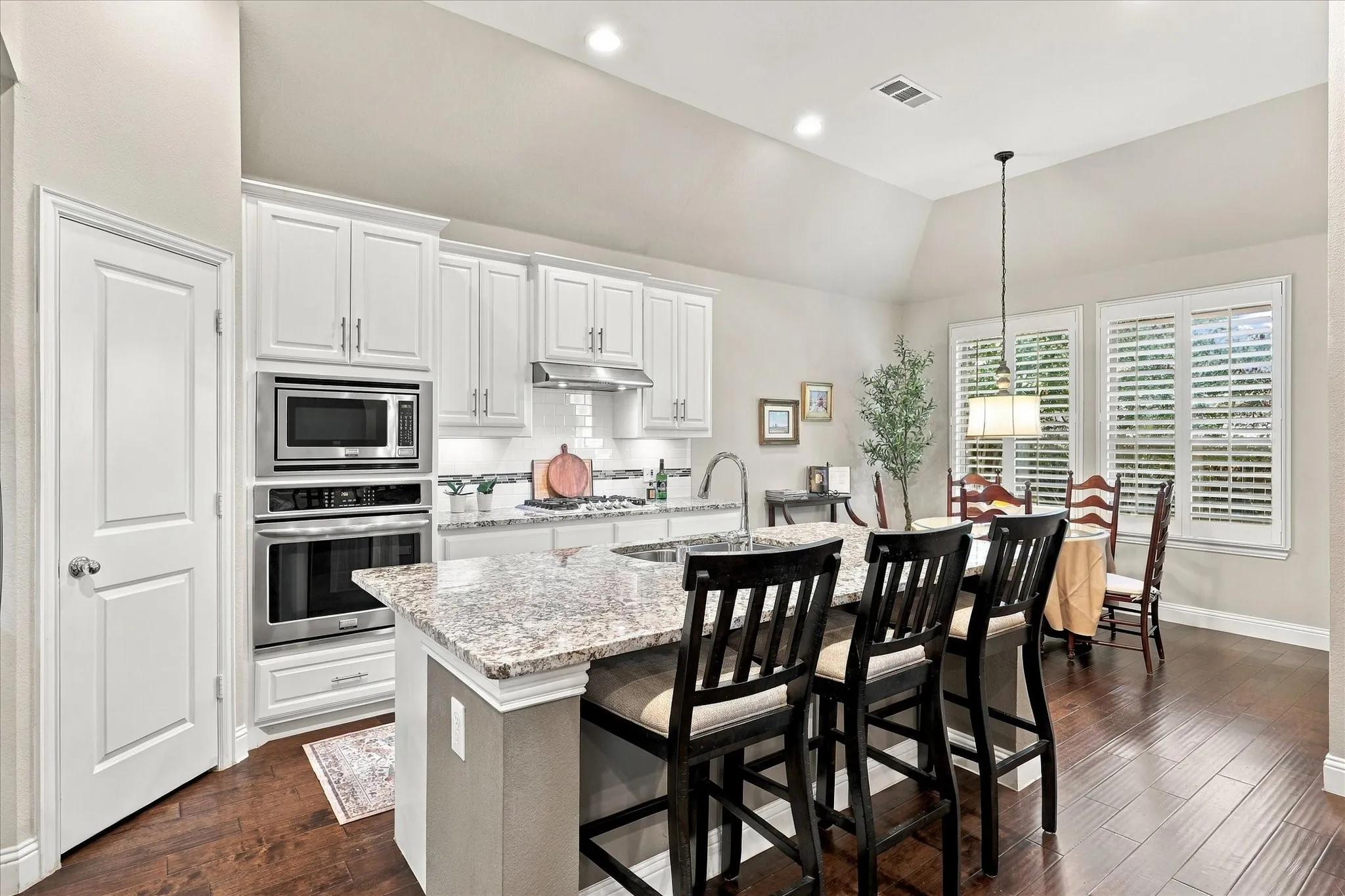 Kitchen featuring white cabinetry, stone-surface island with integrated sink, stainless steel built-in double oven, vaulted ceilings, and dark wood-finish flooring