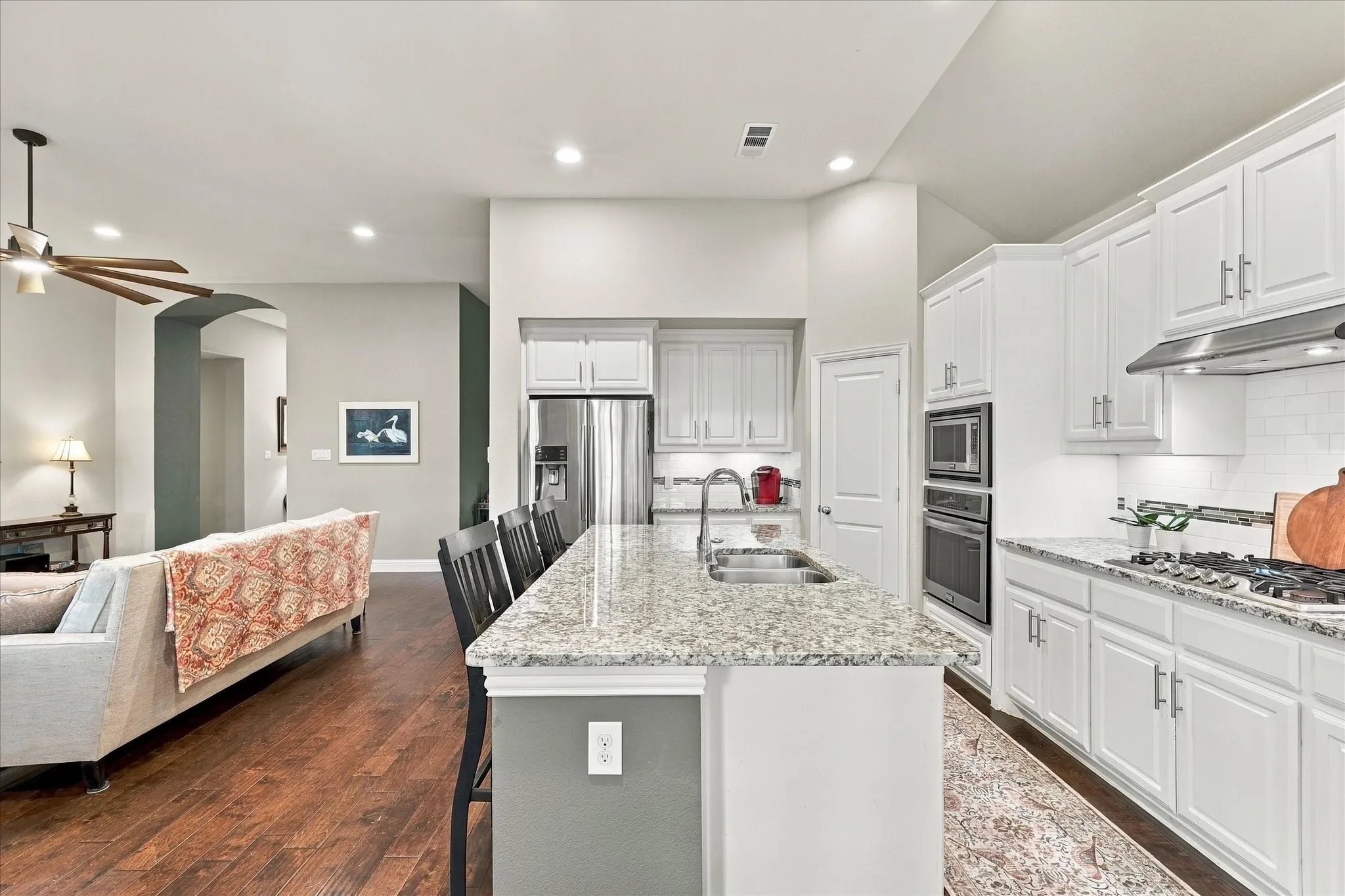 Kitchen featuring a central island with a stone-surface countertop, white cabinetry, integrated stainless steel appliances, and wood-finish flooring