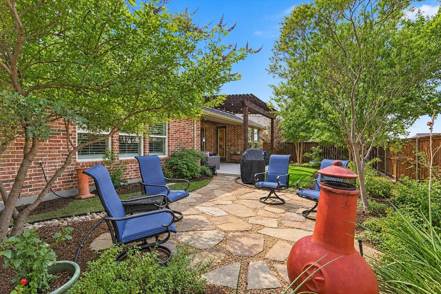 Backyard featuring a flagstone patio, brick exterior, wood pergola, and mature trees
