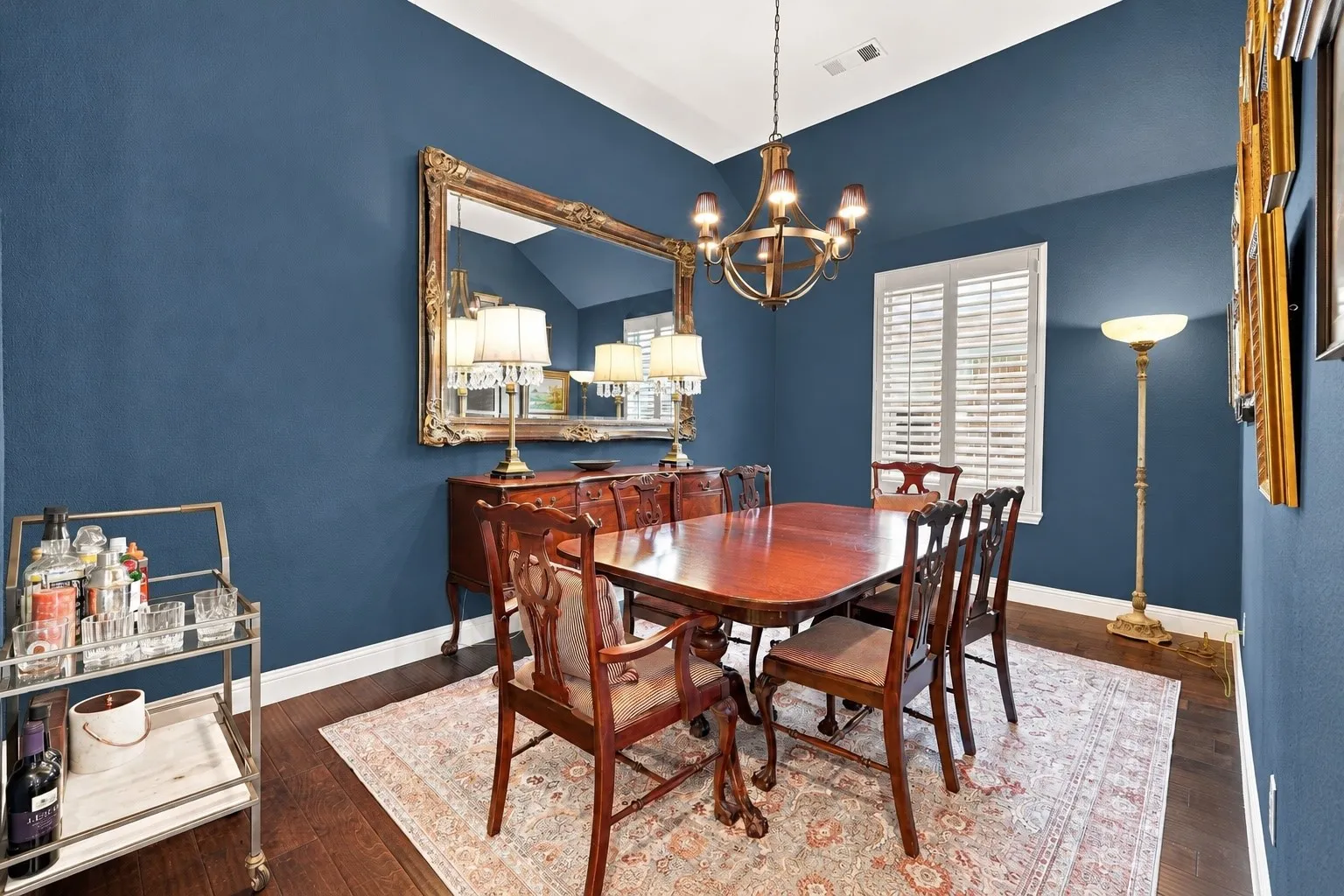 Vaulted ceiling featuring a classic chandelier, dark-toned wood-finish flooring, and white plantation shutters