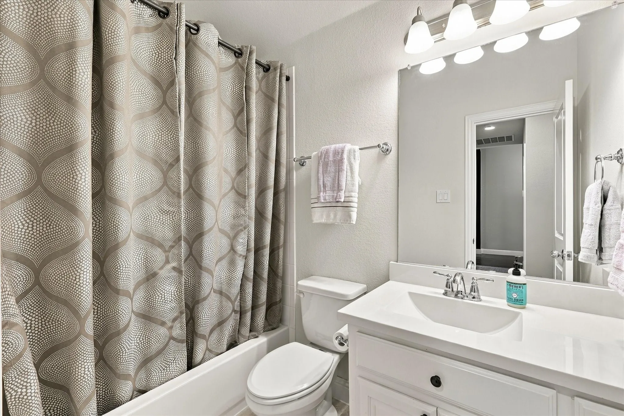 Bathroom featuring a white vanity with a composite countertop and integrated sink, full-width mirror, polished chrome multi-light fixture, and a white porcelain tub with integrated shower surround