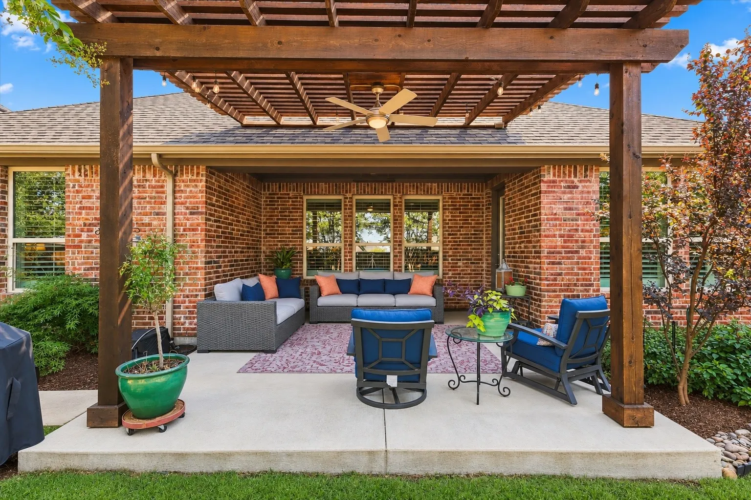 Covered concrete patio featuring a stained wood pergola, ceiling fan, and brick exterior walls