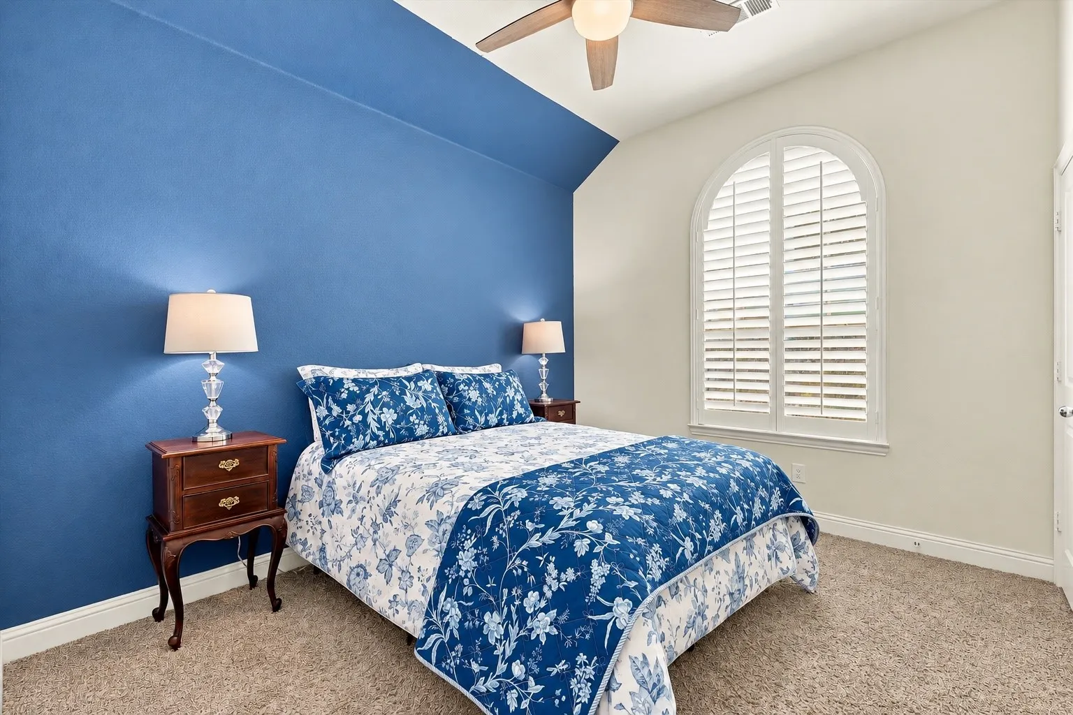 Vaulted ceiling with an integrated wooden ceiling fan, arched window with custom plantation shutters, and a bold accent wall