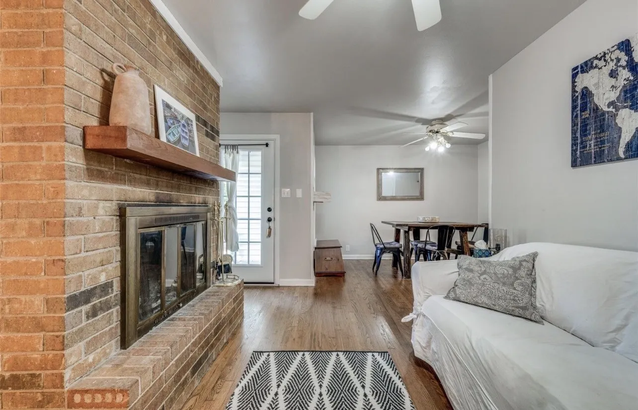 Brick fireplace featuring a wooden mantel and a glass-paneled insert, complemented by wood-finish flooring, ceiling fans, and a glass-paneled exterior door