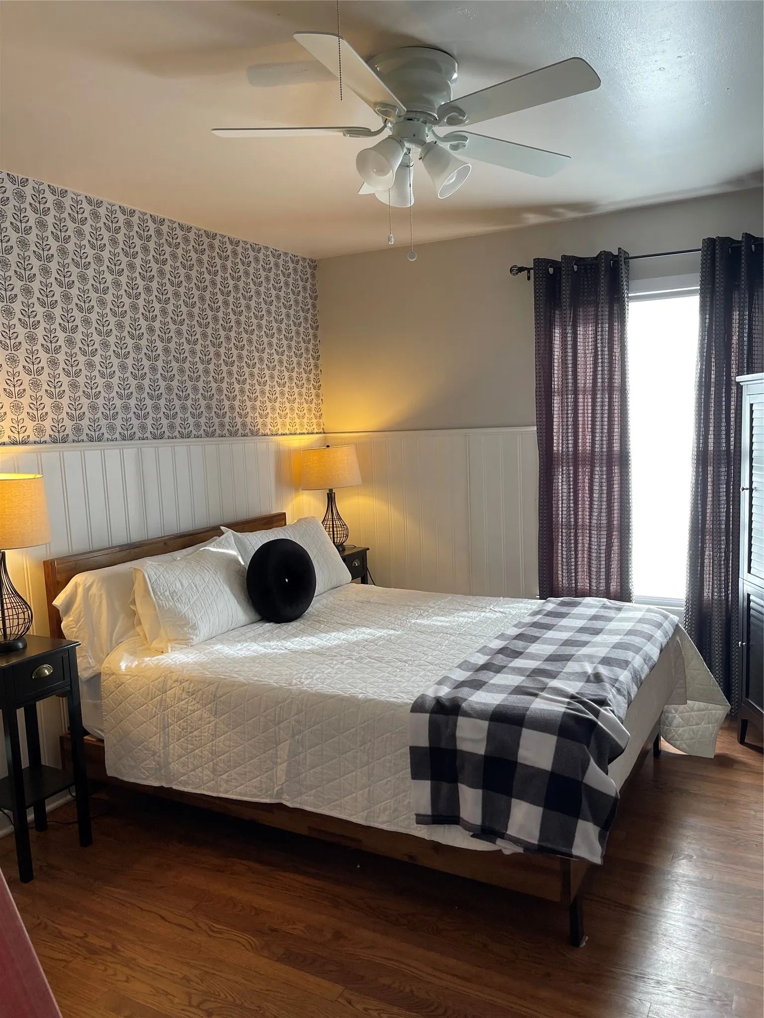 Wood-finish flooring, half-wall beadboard wainscoting, patterned wallpaper accent wall, and a multi-blade ceiling fan with integrated light fixture